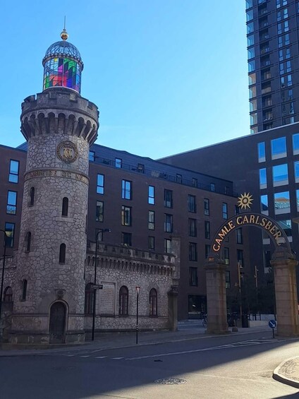 A historic tower with a colorful stained glass dome, a modern building with 'CAMLE CARLSBERG' signage, and a clear blue sky. 1