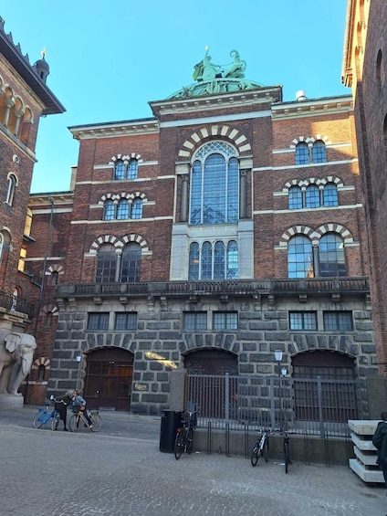 A historic building with arched windows and a central glass facade, surrounded by cobblestone streets and bicycles. 3