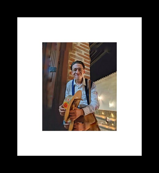 A person holding a wooden shoe with a floral design, standing in front of a brick wall with a metal door. 4