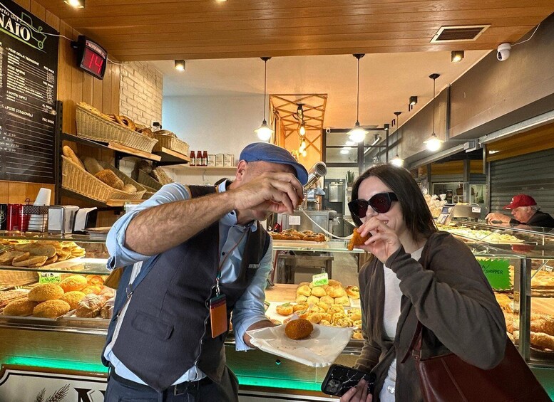 A bakery with various baked goods on display, a digital clock, and a person serving food. 3