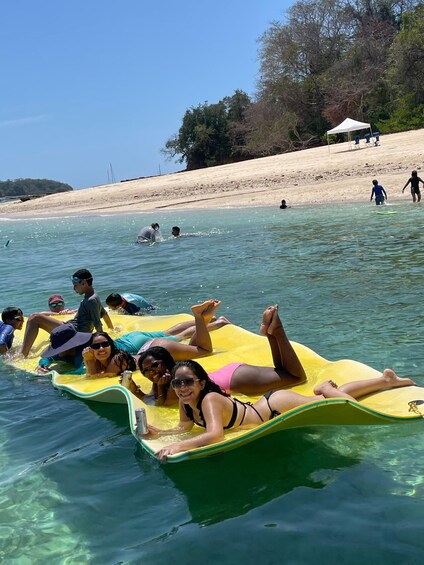 People floating on a yellow raft in clear water, with a beach and trees in the background. 4