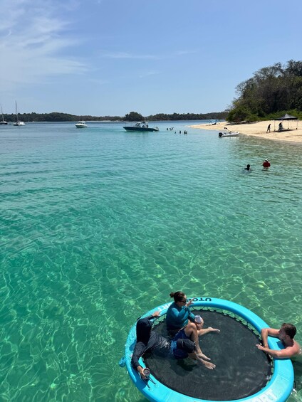 A clear blue sea with a beach, boats, and people swimming and relaxing. 2