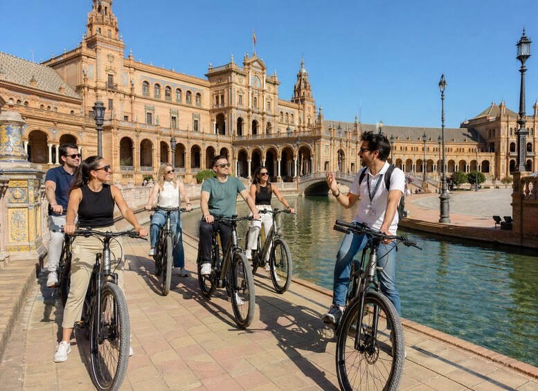 A group of people on bicycles in front of a historic building with arches and a canal. 5