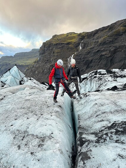 Two people rappelling down a glacier with a mountainous backdrop. 1