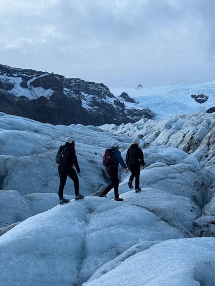 Three hikers on a glacier with snow-covered mountains in the background. 2
