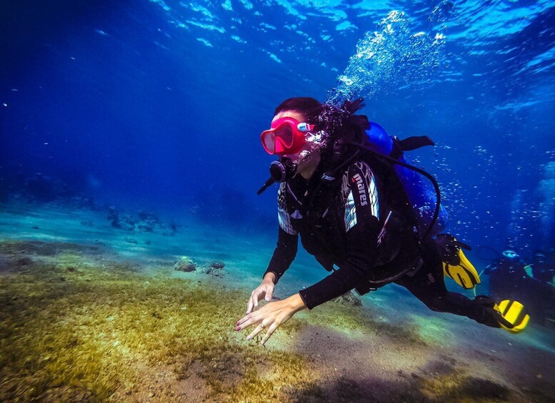 A diver underwater with a snorkel and fins, reaching out towards the sea floor. 1