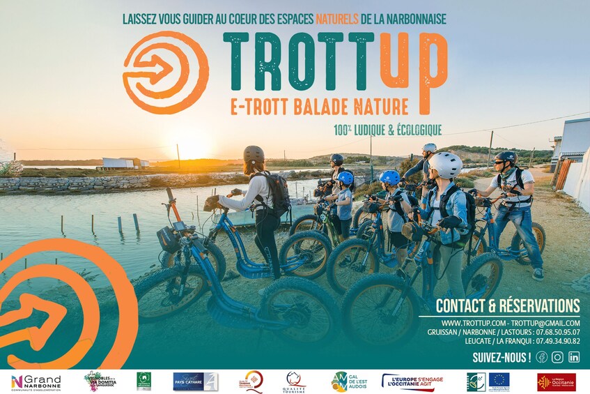A group of people with bicycles in a natural setting, possibly a cycling event, with a body of water and a sunset in the background. 2