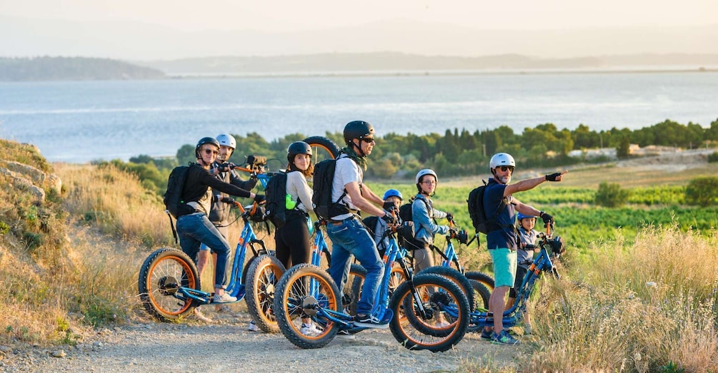 A group of people on mountain bikes on a dirt path with a coastal landscape in the background. 1