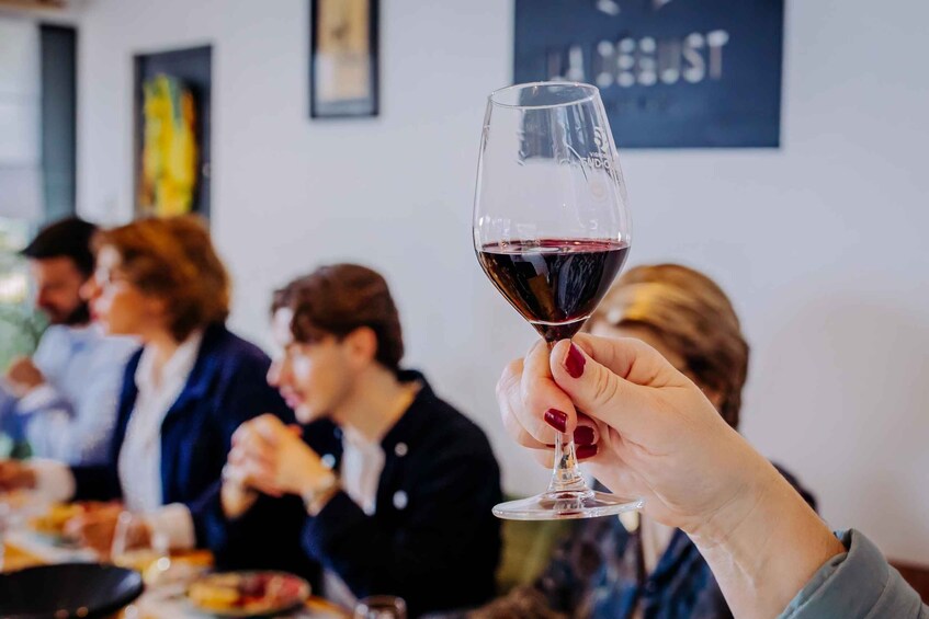 A person holding a wine glass with a dark liquid, presumably wine, at a social gathering. 1