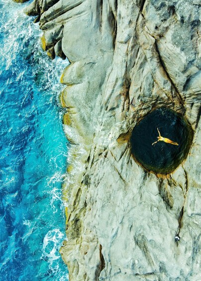 A person swimming in a natural rock pool surrounded by ocean waves. 1