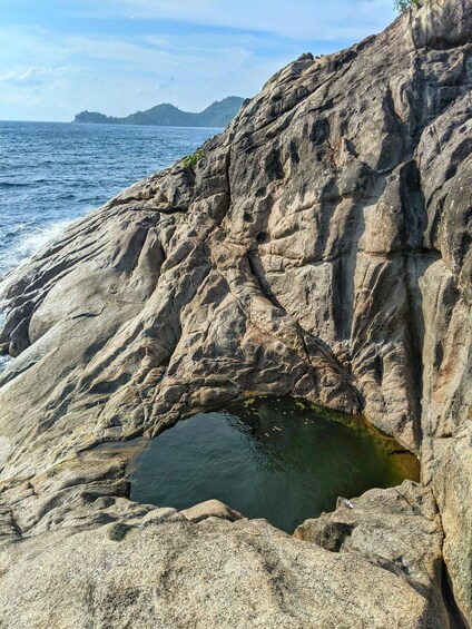 A rocky coastline with a small pool of water and distant mountains. 3