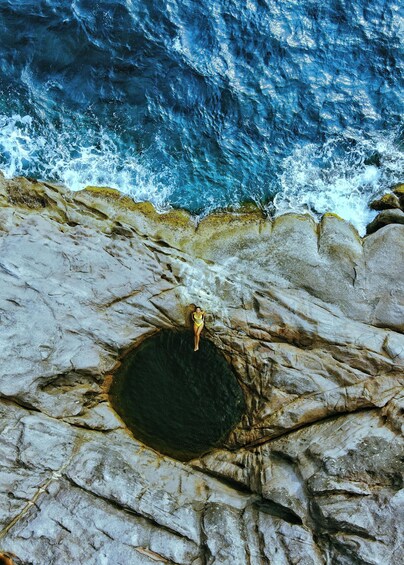 A person in a yellow swimsuit standing in a natural rock formation by the ocean. 5