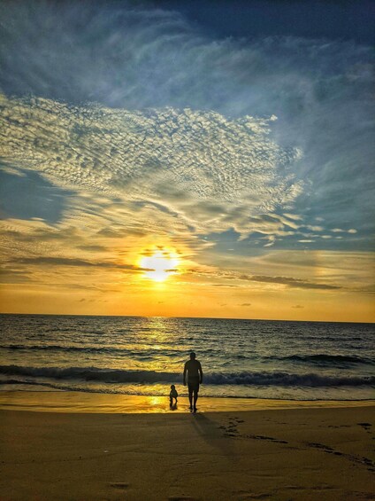 A beach at sunset with a person and a child walking along the shore. 4