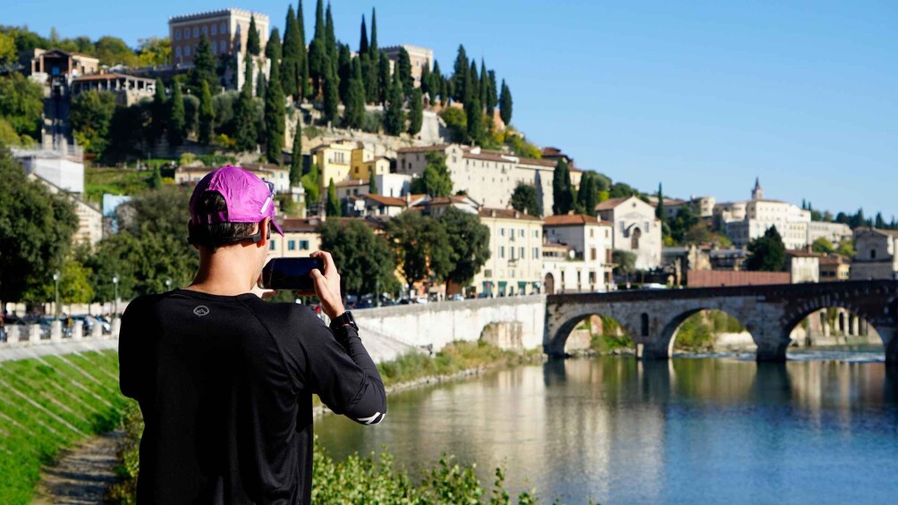 A person taking a photo of a river with a bridge and historic buildings in the background. 1