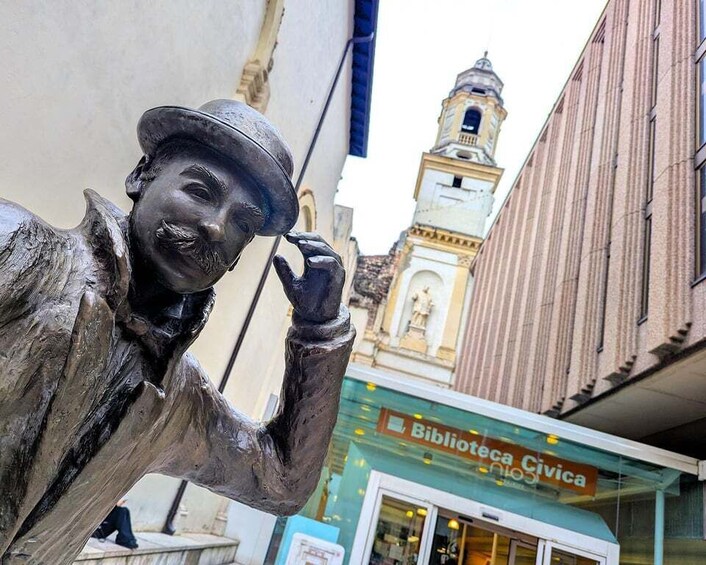 A statue of a man with a hat, a building with a clock tower, and a sign for 'Biblioteca Civica.' 4