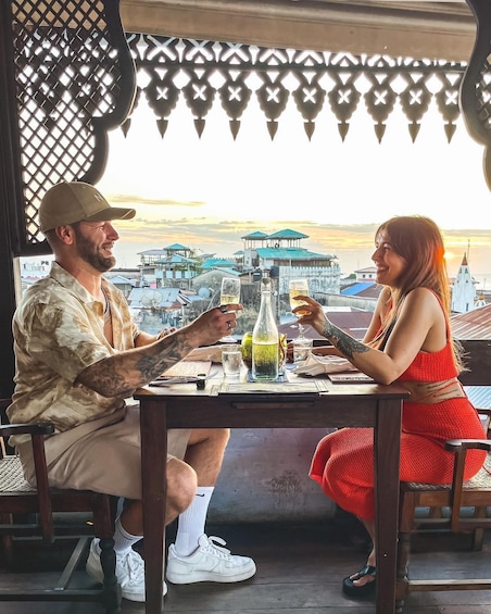 Two people sitting at a table with drinks, overlooking a cityscape with buildings and a church. 4