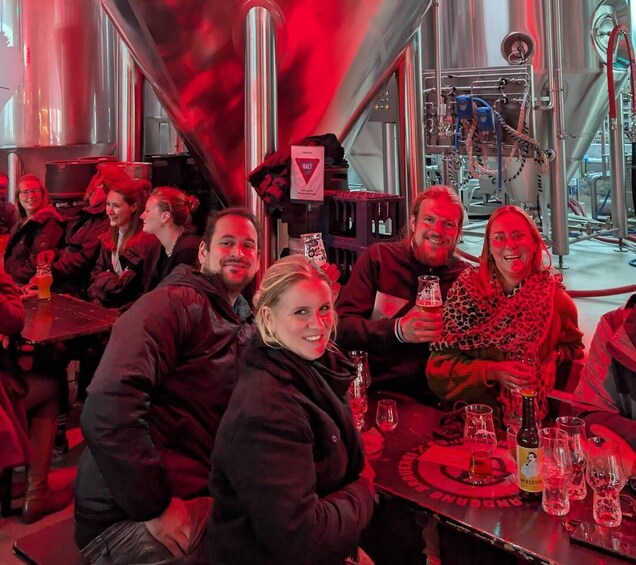 A group of people seated at tables inside a building with industrial equipment and red lighting. 2
