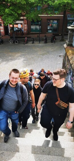 A group of people ascending a stone staircase in an urban setting with brick buildings and greenery in the background. 4