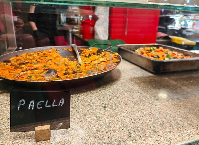 A food display with a sign labeled 'PAELLA' and two pans of food. 1