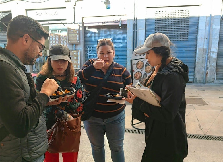 Four people eating street food in an urban setting with closed shops in the background. 3