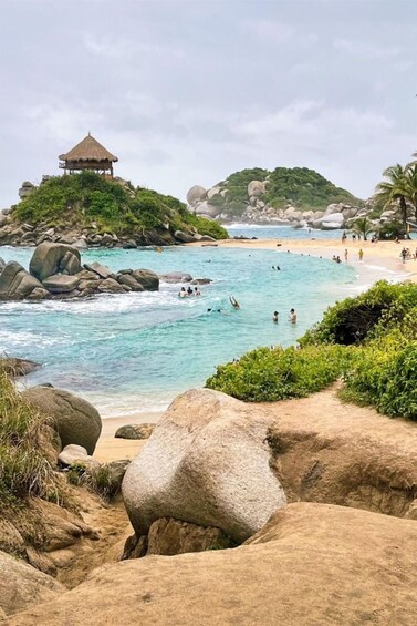A beach with clear turquoise water, large rocks, and a thatched-roof pavilion. 2