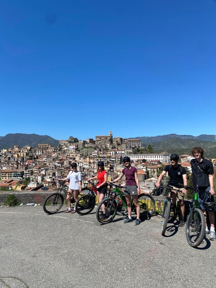 A group of cyclists on a paved area with a cityscape and mountains in the background. 3