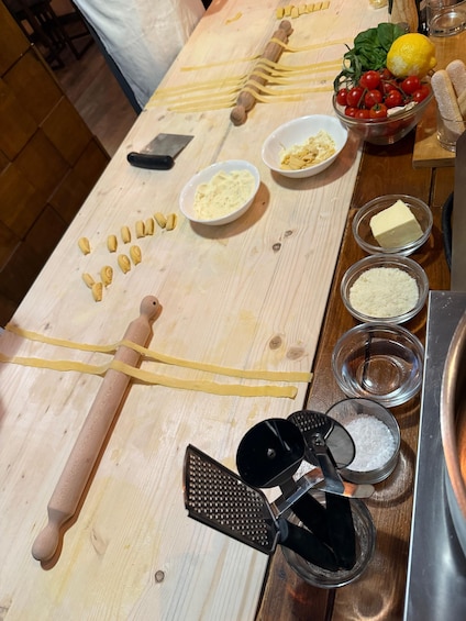 Une table en bois sur laquelle sont disposés des ustensiles pour préparer les pâtes, des ingrédients et des bols. 2