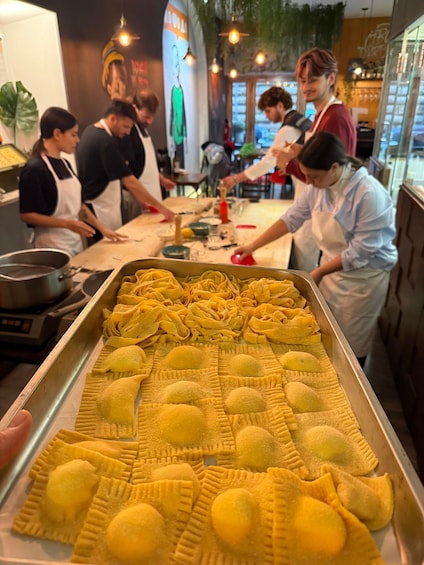 Une cuisine où des chefs préparent des plats, un plateau de raviolis jaunes et une fresque murale. 1