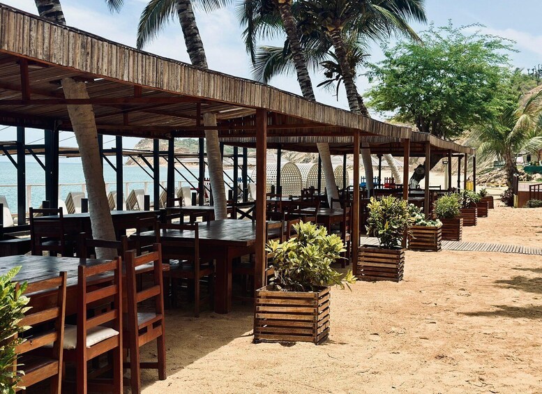 A beachside restaurant with wooden tables and chairs, surrounded by palm trees and overlooking the sea. 4