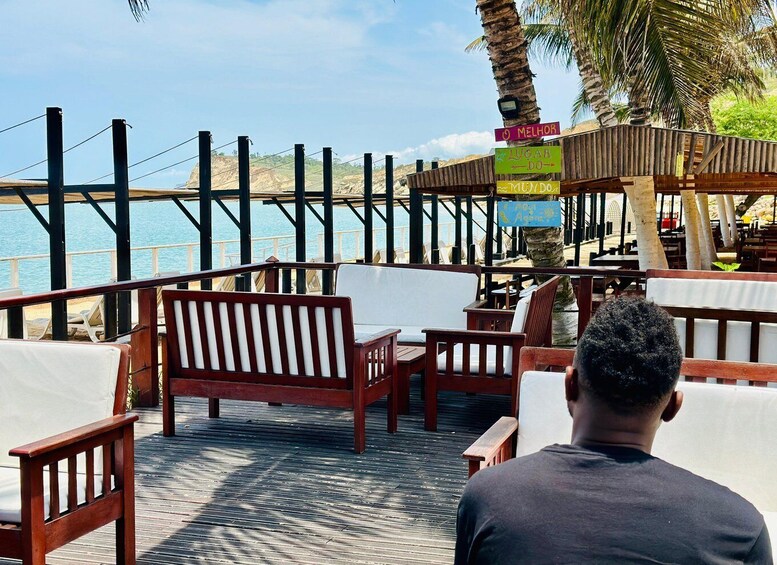 A wooden deck with outdoor seating, palm trees, and a view of the sea. 2
