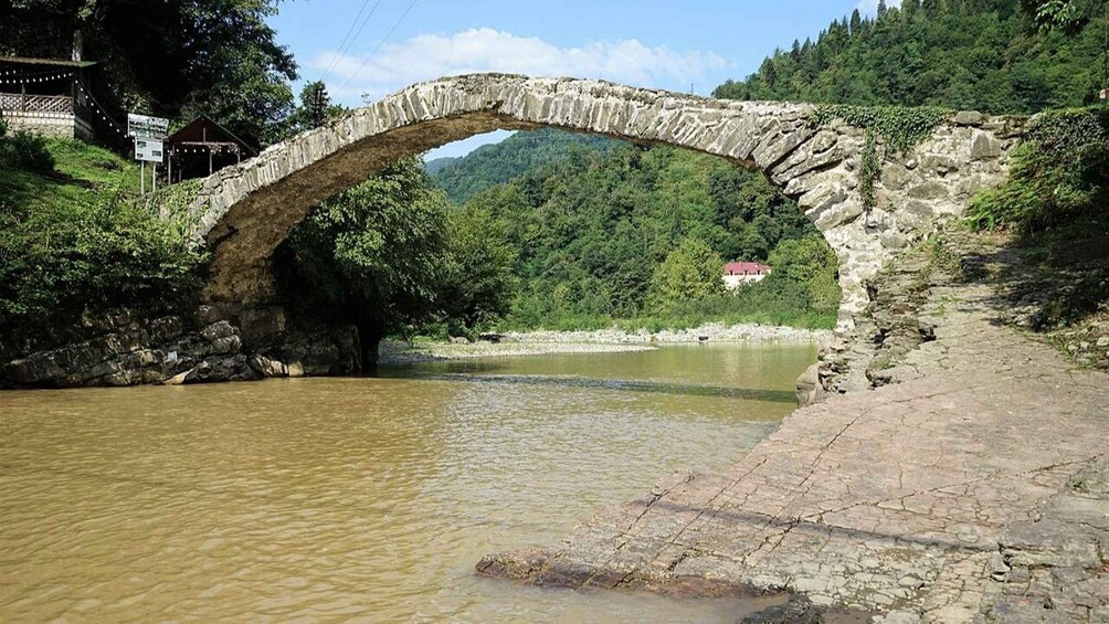 A stone bridge over a river, surrounded by greenery and a hill in the background. 3