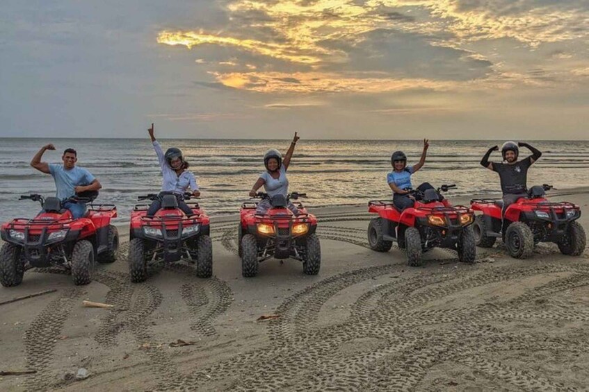 Five people on ATVs on a beach with the ocean in the background. 3