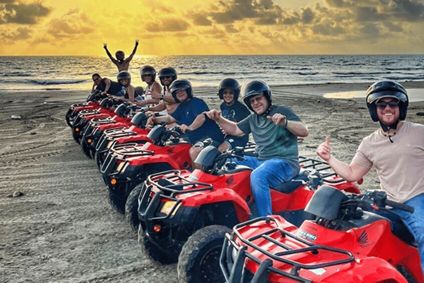 A group of people on red ATVs lined up on a beach with the ocean in the background. 1