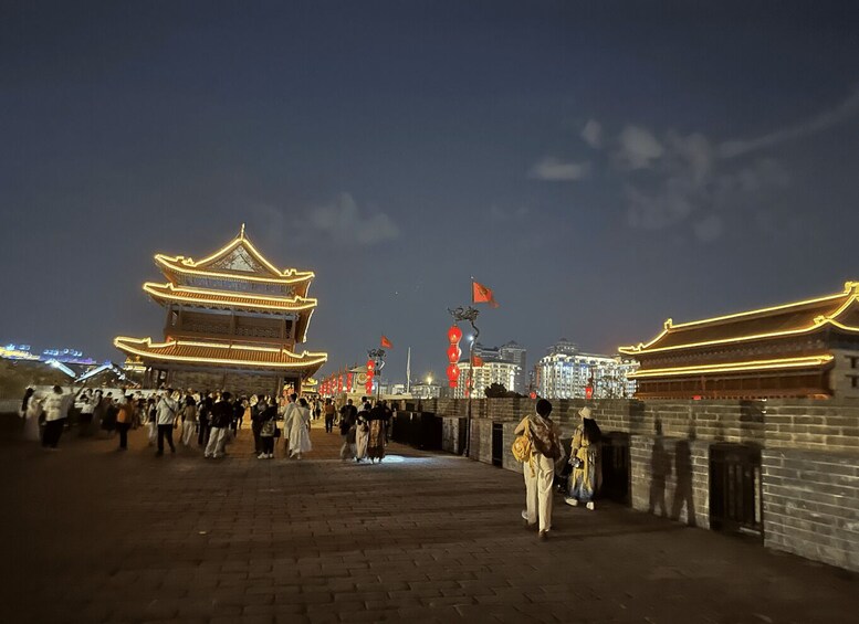 A traditional Chinese building with illuminated rooftops, a crowd of people, and a cityscape in the background. 5
