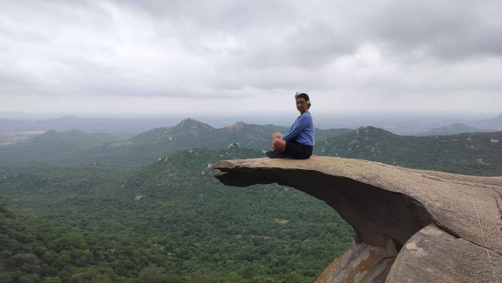A person sitting on a rock ledge overlooking a forested valley. 1