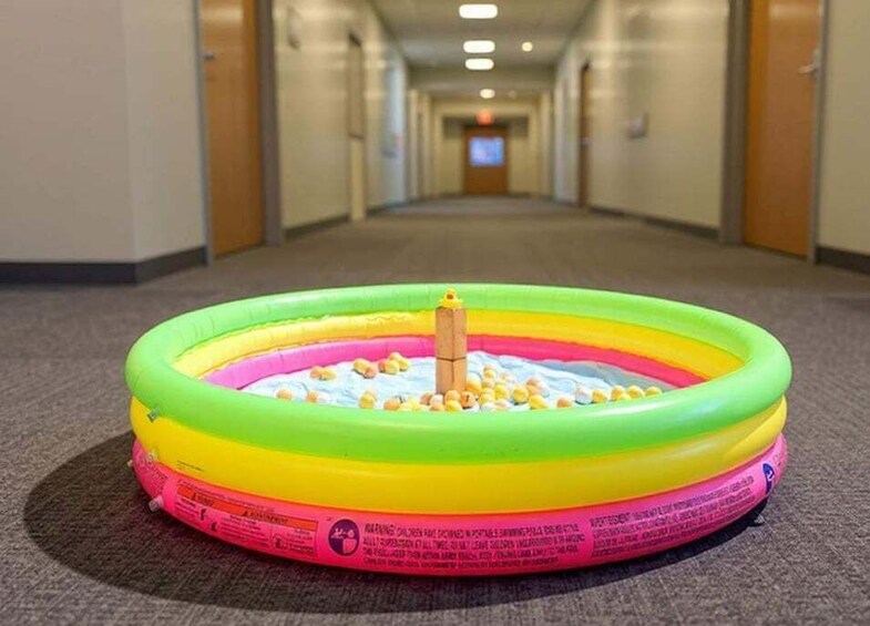A colorful inflatable pool with a yellow float in the middle, placed on a carpeted floor in a hallway. 4