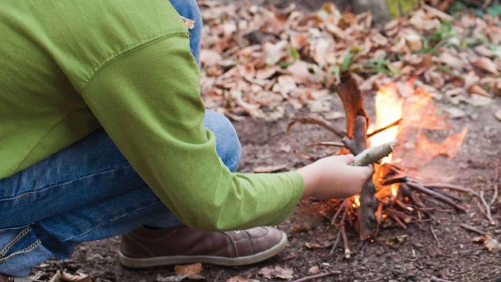 A person crouching by a campfire in a forest. 1