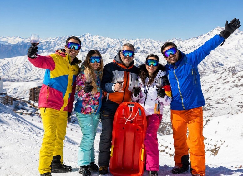 A group of people on a snowy mountain with a clear sky, wearing colorful winter clothing and holding glasses of red wine. 2
