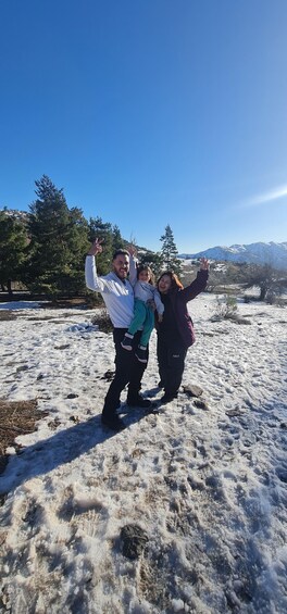 Three people posing in a snowy landscape with trees and mountains in the background. 5