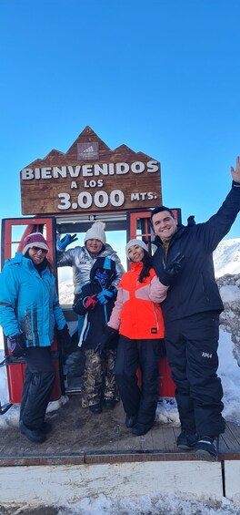 A group of people standing in front of a wooden sign that reads 'BIENVENIDOS A LOS 3.000 MTS.' 1
