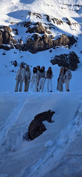 A group of people standing on a snowy mountain slope with rocky outcrops in the background. 4