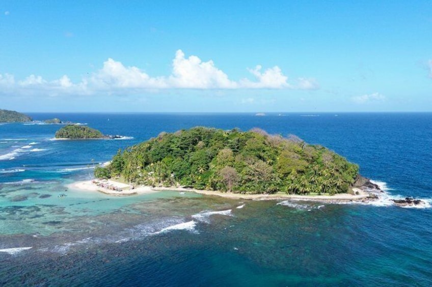A tropical island surrounded by clear blue waters, with a sandy beach and dense green vegetation. 5