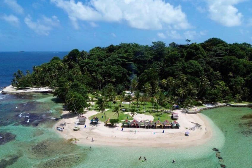 A tropical island with a beach, clear waters, and dense greenery. 1