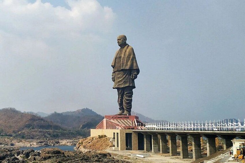 A large statue on a platform with a railing, overlooking a rocky landscape and a body of water. 1