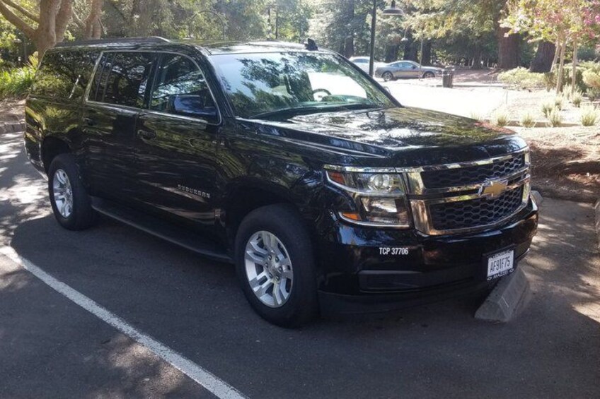 A black SUV parked on a road with trees and a sidewalk in the background. 1