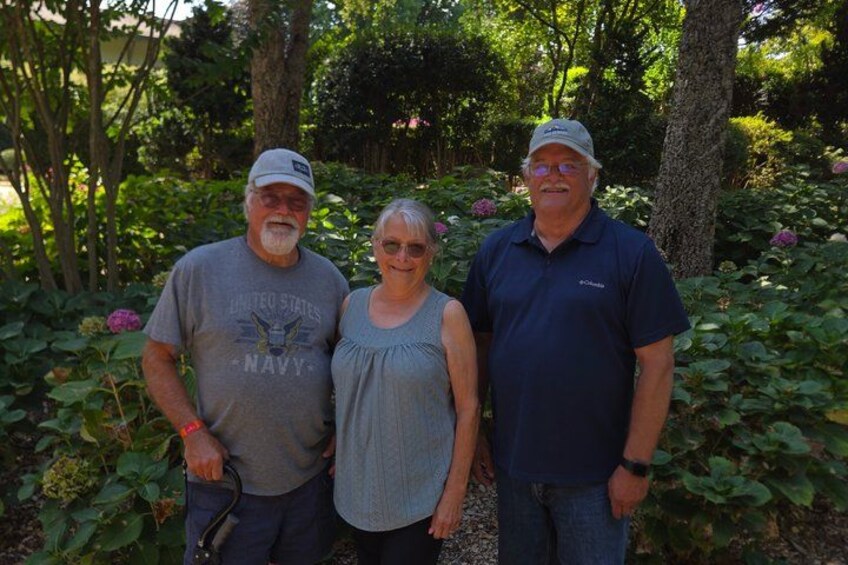 Three people standing in a garden with trees and flowers. 3
