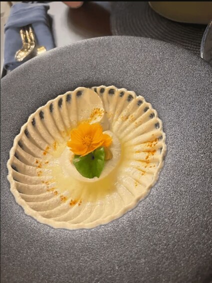 A dessert on a gray plate with a scalloped edge, featuring a yellow flower and green leaves. 3