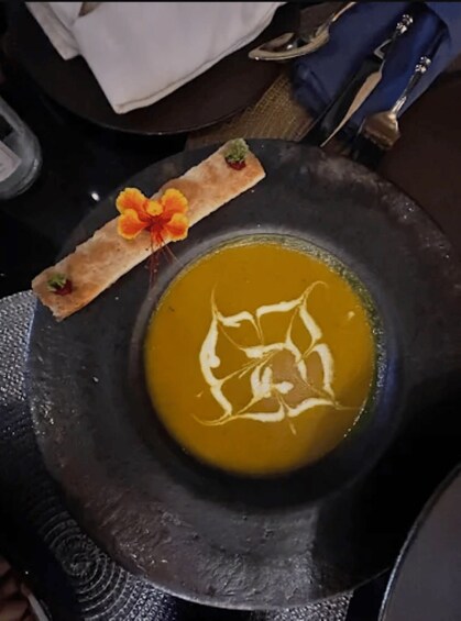 A bowl of soup with a decorative leaf pattern on the surface, accompanied by a small bread roll with a flower on top. 2