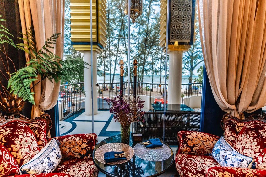 A luxurious lobby with red floral sofas, a glass coffee table, and a view of a balcony with a railing. 4