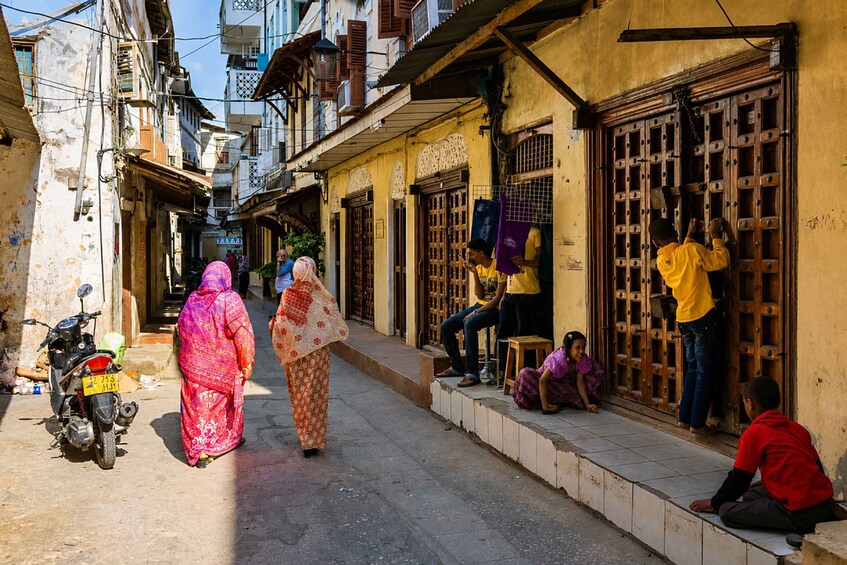 A narrow street with buildings, a motorcycle, and people walking. 5